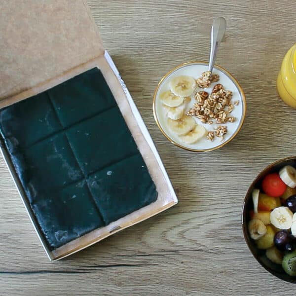 Image d'une boîte de spiruline bio surgelée sur une table de petit déjeuner, à côté d'une salade de fruits colorée, offrant une option nutritive pour bien commencer la journée.