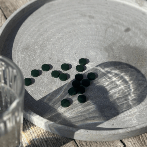 Comprimés de spiruline bio Etika Spirulina exposés au soleil, à côté d’un verre d’eau prêt pour la prise
