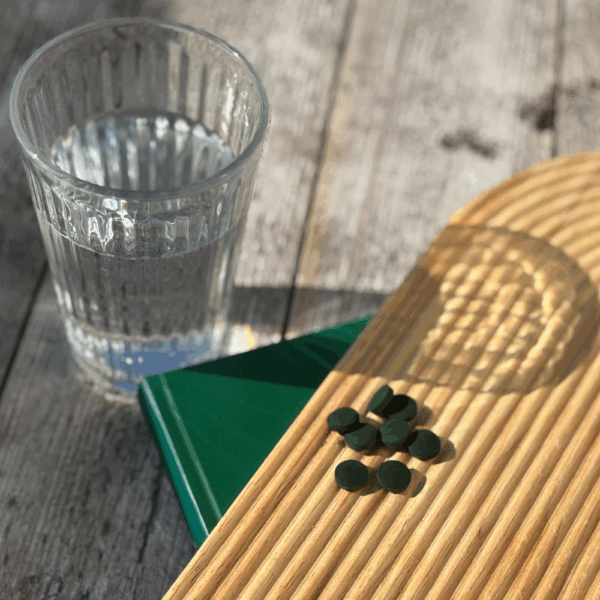 Comprimés de spiruline bio Etika Spirulina exposés au soleil, à côté d’un verre d’eau prêt pour la prise